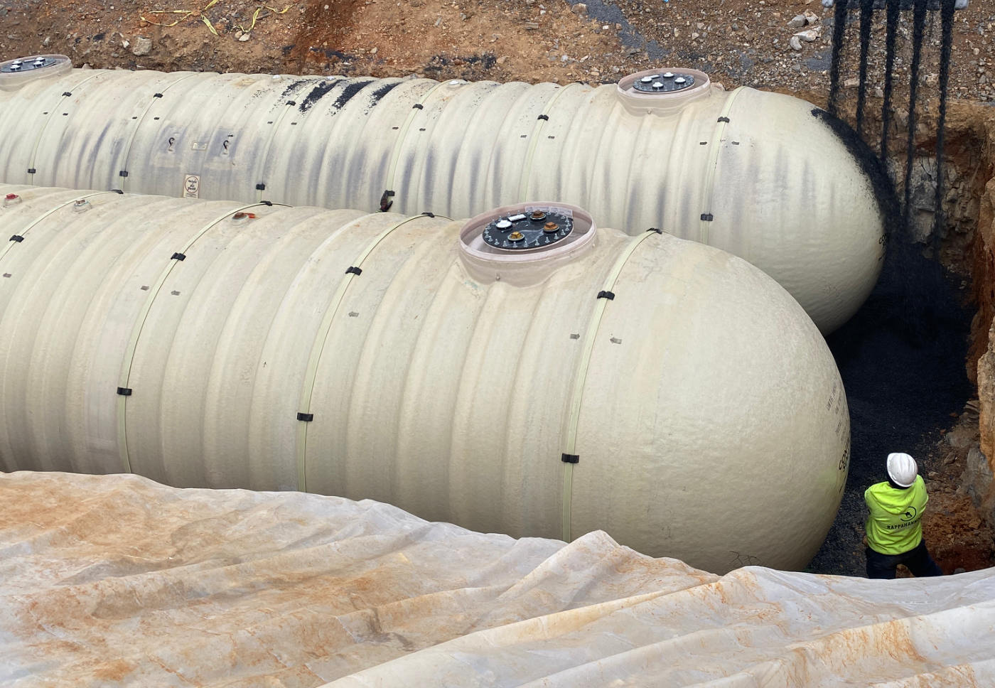 Crew member guiding pea-gravel backfill around fiberglass tanks