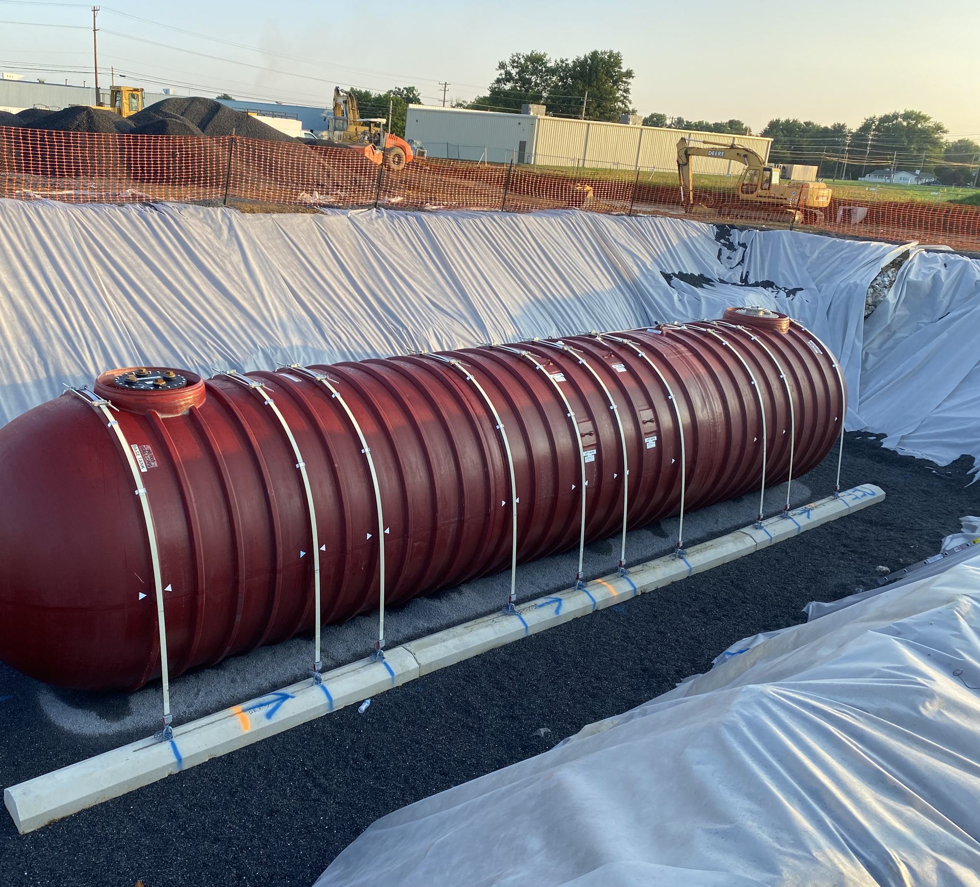 Hold-down straps over a tank set on concrete deadmen in a fabric-lined excavation