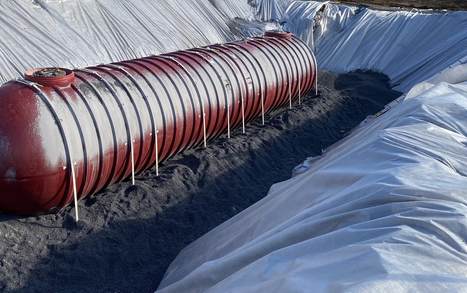 Red underground storage tank set on bedding in a fabric-lined excavation